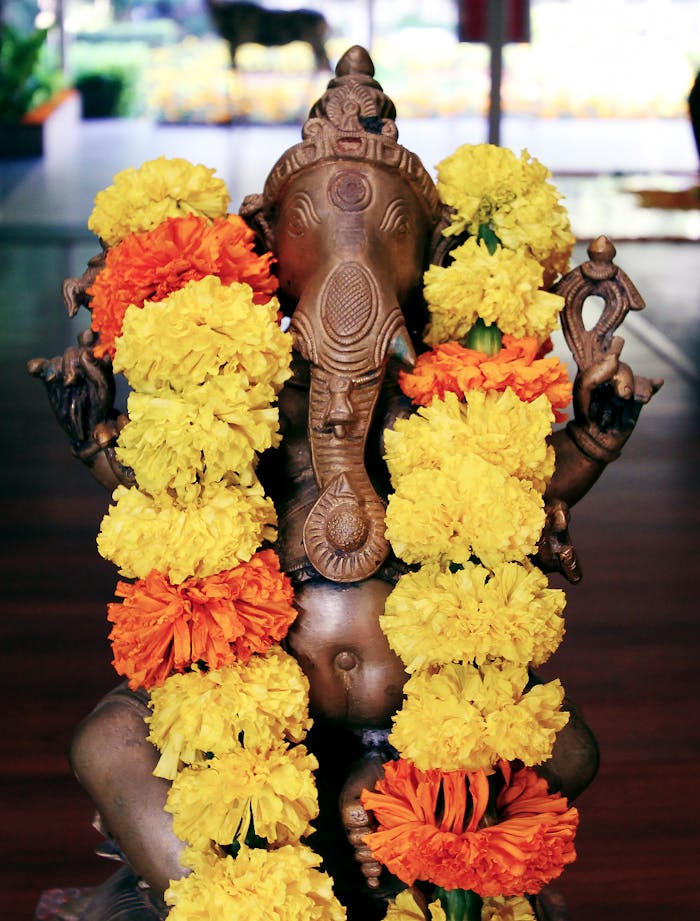 A brass Ganesha idol adorned with vibrant yellow and orange marigold garlands, symbolizing spirituality.